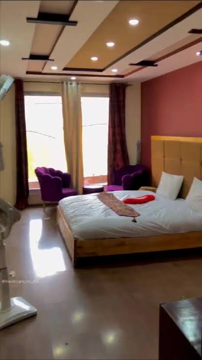 Deluxe Double Room with a made bed, reading chair and a wide window facing the mountains